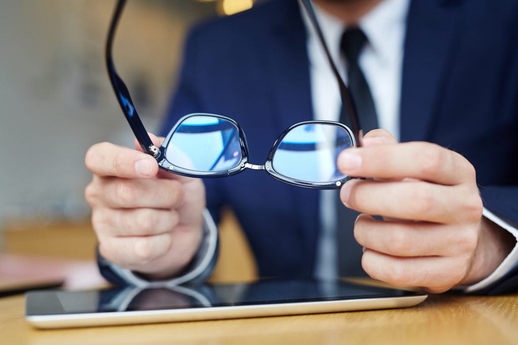 Human hands holding eyeglasses over touchpad